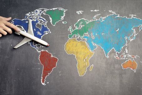 Continent - Top view of crop anonymous person holding toy airplane on colorful world map drawn on chalkboard