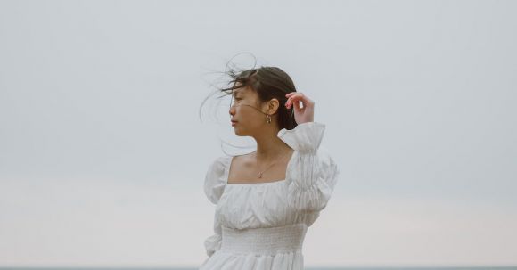 Lone Traveler - Gentle Asian traveler in white dress contemplating sea