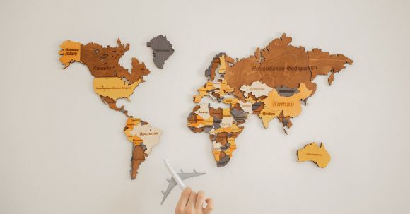 Continent - Crop unrecognizable person with toy aircraft near multicolored decorative world map with continents attached on white background in light studio