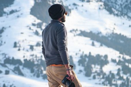 Exploration - Man Wearing Gray Long-sleeved Shirt and Brown Shorts Holding Black Dslr Camera on Mountain
