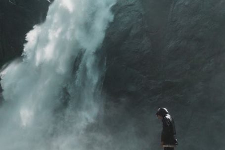 Exploration - Man Standing on Brown Rock Cliff in Front of Waterfalls Photography
