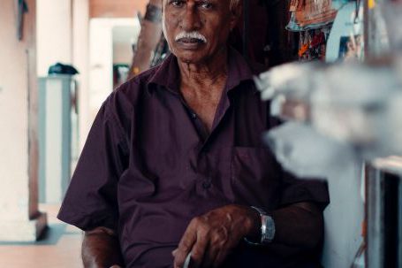 Local Fairs - Serious elderly Indian male in shirt sitting in street market with magazines while looking at camera in daylight