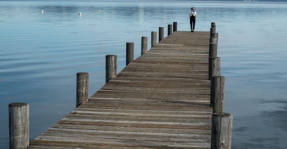 Lone Traveler - Distant traveler standing in solitude on long wooden pier with landscape of calm lake in highlands