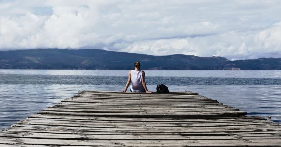 Solo Nature - Person Sitting on Brown Wooden Dock Under Cloudy Blue Sky
