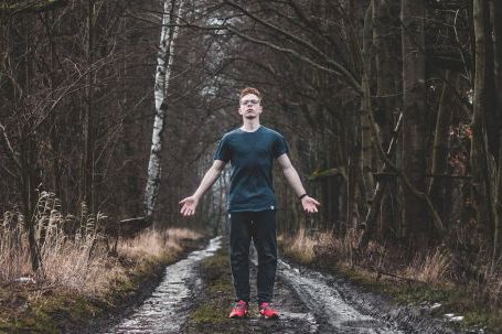 Solo Nature - Man Wearing Black Crew Neck T-shirt and Black Pants Standing on Pathway Between Bare Trees